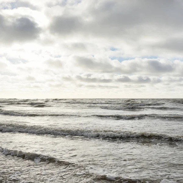 Fırtınadan sonra Baltık Denizi. Dramatik gökyüzü, parlayan bulutlar, yumuşak güneş ışığı. Dalgalar, su sıçratma. Resimli manzara, deniz manzarası, doğa. Panoramik görünüm