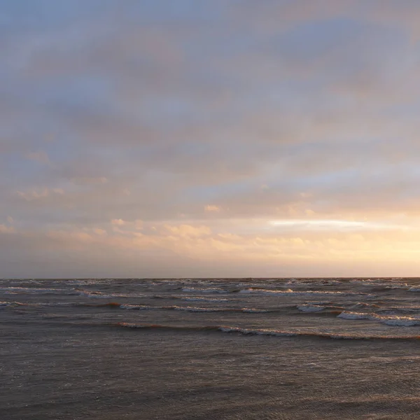 Fırtınadan sonra gün batımında Baltık Denizi. Dramatik gökyüzü, parlayan bulutlar, dofty altın güneş ışığı, dalgalar, fışkıran su. Resimli panoramik manzara. Doğa, çevre, ekoloji
