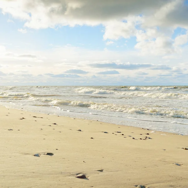 Kumlu bir sahilden (kum tepeleri) Baltık denizinin panoramik görüntüsü. Parlayan bulutlarla, dalgalarla ve su sıçramalarıyla berrak bir gökyüzü. Idyllic deniz manzarası. Sıcak kış havası, iklim değişikliği, doğa