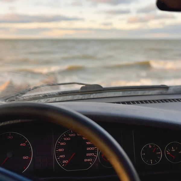 Baltic sea shore at sunset. Soft sunlight, clear sky with glowing clouds, waves and water splashes. Idyllic seascape. Latvia, Europe. View from the car. Local travel, ecotourism, wanderlust concepts