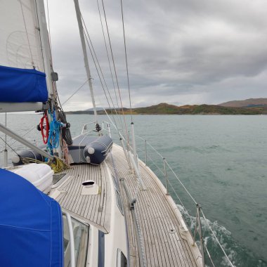 Kayalık göl kıyısında seyir halindeki ahşap meşe güvertesiyle donatılmış bir yat. İskoçya, İngiltere. Denizcilik gemisi, ulaşım, spor, eğlence aktivitesi, yelkenli yarışı, seyahat, seyahat