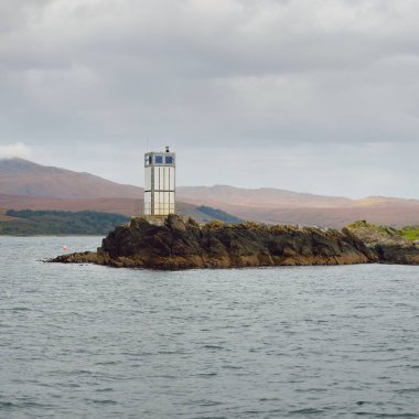 Rocky gölü kıyıları, dağ zirveleri, dağlar, vadiler ve tepeler. Deniz feneri. Yelkenliden panoramik manzara. Dramatik bir gökyüzü. İskoçya, İngiltere. Atmosferik manzara. Seyahat yerleri, yürüyüş, eko-turizm