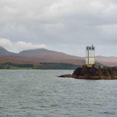 Rocky gölü kıyıları, dağ zirveleri, dağlar, vadiler ve tepeler. Deniz feneri. Yelkenliden panoramik manzara. Dramatik bir gökyüzü. İskoçya, İngiltere. Atmosferik manzara. Seyahat yerleri, yürüyüş, eko-turizm