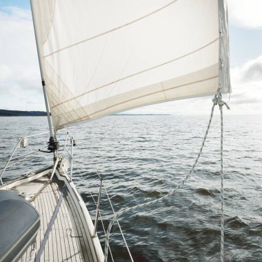 Kayalık göl kıyılarında seyir halindeki ahşap meşe güvertesiyle donatılmış modern bir yat. İskoçya, İngiltere. Güverteden pruvaya, direğe, yelkenlere bakın. Seyahat tutkusu, eğlence aktivitesi, spor, yelkenli yarışı, deniz yolculuğu.