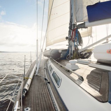 Kayalık göl kıyılarında seyir halindeki ahşap meşe güvertesiyle donatılmış modern bir yat. İskoçya, İngiltere. Güverteden pruvaya, direğe, yelkenlere bakın. Seyahat tutkusu, eğlence aktivitesi, spor, yelkenli yarışı, deniz yolculuğu.