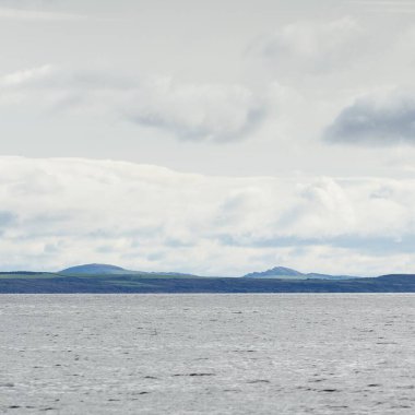 İskoçya, Rothesay 'ın kayalık kıyıları, tepeleri ve vadileri üzerinde dramatik bir gökyüzü. Yelkenliden panoramik manzara. Seyahat merkezleri, turizm, yürüyüş, dönüm noktası, ekoloji, çevre, doğa temaları
