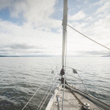 Kayalık göl kıyılarında seyir halindeki ahşap meşe güvertesiyle donatılmış modern bir yat. İskoçya, İngiltere. Güverteden pruvaya, direğe, yelkenlere bakın. Seyahat tutkusu, eğlence aktivitesi, spor, yelkenli yarışı, deniz yolculuğu.