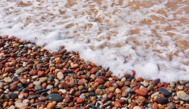 Islak çakıl taşları. Deniz kıyısı, sahil. Deniz suyu yüzeyi, dalgalar. Su sıçratma, köpük. Doğal doku, arka plan, duvar kağıdı, desen. Kavramsal yaz sahnesi. Doğa, tatiller, rahatlama, meditasyon kavramları