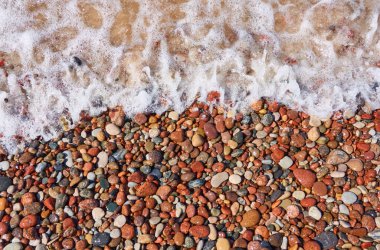 Islak çakıl taşları. Deniz kıyısı, sahil. Deniz suyu yüzeyi, dalgalar. Su sıçratma, köpük. Doğal doku, arka plan, duvar kağıdı, desen. Kavramsal yaz sahnesi. Doğa, tatiller, rahatlama, meditasyon kavramları