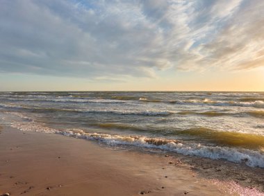 Fırtınadan sonra Baltık kıyıları (kum tepeleri, plaj). Gün batımı, yumuşak altın güneş ışığı, parlayan bulutlar. Resimli panoramik manzara. Doğa, çevre, ekoloji, eko-turizm, yürüyüş, keşif kavramları