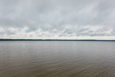 Kristal berrak bir orman gölü (nehir) kıyısından panoramik manzara. Dramatik gökyüzü, parlayan fırtına bulutları. Idyllic manzara. İlkbahar, yazın başı. Doğa, çevre, ekoloji, eko-turizm, yürüyüş