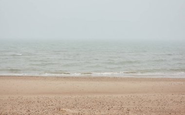 Kalın bir siste Baltık Denizi kıyısında. Kumsal, kum tepeleri. Yağmurlu bir gün, kasvetli bir gökyüzü, yumuşak bir güneş ışığı. Deniz Burnu. Doğa, çevre, tatiller, eko-turizm, yürüyüş, keşif kavramları. Panoramik görünüm