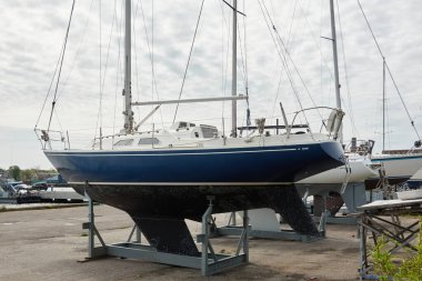 Mavi yelkenli donanımlı yelkenli bir yat kulübünde karada duruyor. Hizmet, onarım, ulaşım, spor, eğlence, eğlence aktivitesi