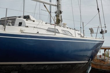 Mavi yelkenli donanımlı yelkenli bir yat kulübünde karada duruyor. Hizmet, onarım, ulaşım, spor, eğlence, eğlence aktivitesi