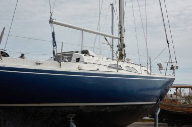 Mavi yelkenli donanımlı yelkenli bir yat kulübünde karada duruyor. Hizmet, onarım, ulaşım, spor, eğlence, eğlence aktivitesi