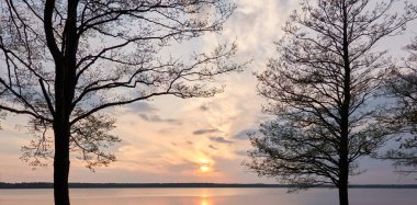 Gün batımında Orman Gölü. Ağaç siluetleri. Yumuşak güneş ışığı, parlayan bulutlar, kristal berrak suda yansıma. Idyllic manzara. Panoramik manzara. Doğa, ekoloji, çevre turizmi. Barış ve neşe kavramları