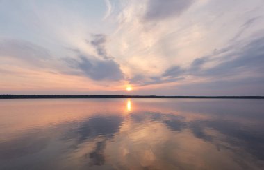 Gün batımında Orman Gölü. Yumuşak güneş ışığı, parlayan pembe ve altın bulutlar, kristal berrak bir suda yansıma. Idyllic manzara. Panoramik manzara. Doğa, ekoloji, çevrecilik. Barış ve neşe kavramları