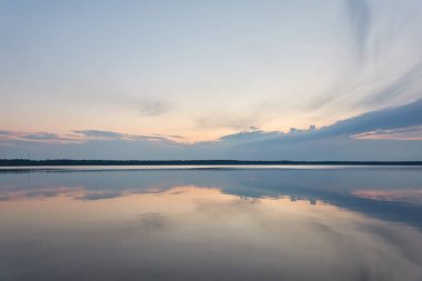 Gün batımında Orman Gölü. Yumuşak güneş ışığı, gece yarısı güneşi, parlayan bulutlar, kristal berrak bir suda yansıma. Idyllic manzara. Panoramik manzara. Doğa, ekoloji, çevre turizmi. İlkbahar, yazın başı