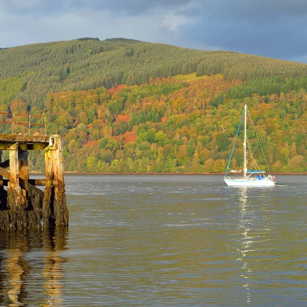 Sailboat anchored in lake. Majestic forest hills. Scotland, UK. Atmospheric landscape. Travel destinations, sailing, cruising, eco tourism, hiking, nature, environmental conservation