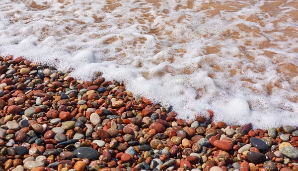Islak çakıl taşları. Deniz kıyısı, sahil. Deniz suyu yüzeyi, dalgalar. Su sıçratma, köpük. Doğal doku, arka plan, duvar kağıdı, desen. Kavramsal yaz sahnesi. Doğa, tatiller, rahatlama, meditasyon kavramları