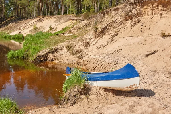 Blue canoe standing near the sandy shore (beach) of the Irbe river. Kurzeme, Latvia. Nature, ecology, eco tourism, hiking, leisure activity, boating, rowing, sport, healthy lifestyle, wanderlust