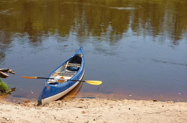 Blue canoe standing near the sandy shore (beach) of the Irbe river. Kurzeme, Latvia. Nature, ecology, eco tourism, hiking, leisure activity, boating, rowing, sport, healthy lifestyle, wanderlust