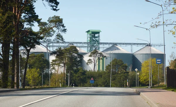 Modern grain elevator in cargo port. Asphalt road (highway), bus stop. Ventspils, Latvia. Concept urban landscape. Nature, ecology, biotechnology, rapeseed fuel, environment, ecological damage themes