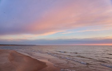 Gün batımında Baltık kıyısı. Kumsal, kum tepeleri. Dramatik gökyüzü, mavi ve pembe parlayan bulutlar, yumuşak altın güneş ışığı, gece yarısı güneşi. Deniz manzarası, bulut manzarası, doğa. Panoramik görünüm