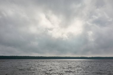 Kristal berrak bir orman gölü (nehir) kıyısından panoramik manzara. Dramatik gökyüzü, parlayan fırtına bulutları. Idyllic manzara. İlkbahar, yazın başı. Doğa, çevre, ekoloji, eko-turizm, yürüyüş