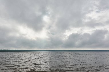 Kristal berrak bir orman gölü (nehir) kıyısından panoramik manzara. Dramatik gökyüzü, parlayan fırtına bulutları. Idyllic manzara. İlkbahar, yazın başı. Doğa, çevre, ekoloji, eko-turizm, yürüyüş