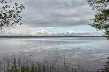 Kristal berrak bir orman gölü (nehir) kıyısından panoramik manzara. Dramatik gökyüzü, parlayan fırtına bulutları. Idyllic manzara. İlkbahar, yazın başı. Doğa, çevre, ekoloji, eko-turizm, yürüyüş