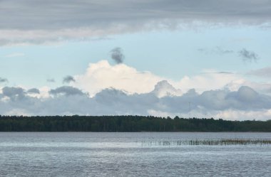 Kristal berrak bir orman gölü (nehir) kıyısından panoramik manzara. Dramatik gökyüzü, parlayan fırtına bulutları. Idyllic manzara. İlkbahar, yazın başı. Doğa, çevre, ekoloji, eko-turizm, yürüyüş