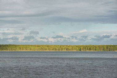 Kristal berrak bir orman gölü (nehir) kıyısından panoramik manzara. Dramatik gökyüzü, parlayan fırtına bulutları. Idyllic manzara. İlkbahar, yazın başı. Doğa, çevre, ekoloji, eko-turizm, yürüyüş