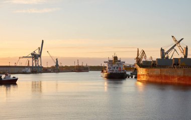 Liman terminaline büyük bir kargo gemisi yükleniyor. Gün batımı. Yük taşımacılığı, deniz taşımacılığı, lojistik, küresel iletişim, dünya çapında taşımacılık, ekonomi, ticaret, sanayi