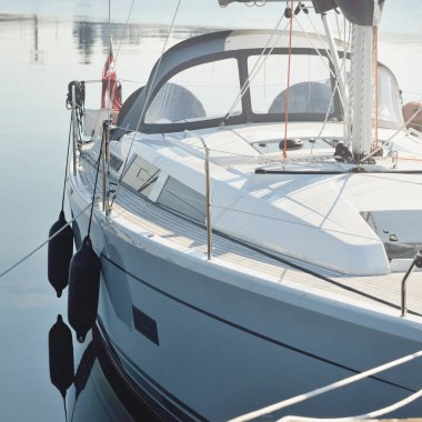 Beyaz modern yelkenli (kiralık ve satılık) yat limanındaki bir rıhtıma demirlemiş. Tahta meşe güvertesi. Denizcilik, ulaşım, amatör yelkencilik, tatiller, gezinti, eğlence kavramları