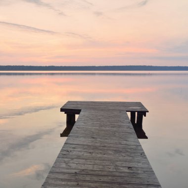 Forest lake at sunset. Wooden pier. Soft sunlight, glowing clouds, symmetry reflections in a crystal clear water. Idyllic landscape. Panoramic view. Nature, ecology, ecotourism. Peace and joy concepts