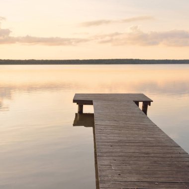 Forest lake (river) at sunset. Wooden pier. Glowing clouds, symmetry reflections in a still crystal clear water. Idyllic landscape. Nature, ecology, ecological reserve, ecotourism, hiking, vacations