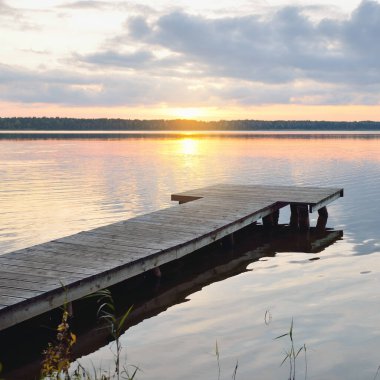 Forest lake (river) at sunset. Wooden pier. Glowing clouds, symmetry reflections in a still crystal clear water. Idyllic landscape. Nature, ecology, ecological reserve, ecotourism, hiking, vacations
