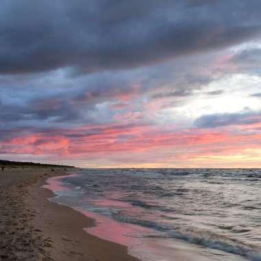 Gün batımında Baltık kıyılarından panoramik manzara. Dramatik fırtına gökyüzü, parlayan bulutlar, altın güneş ışığı. Dalgalar, su sıçratma. Doğa, çevre, kararsız hava