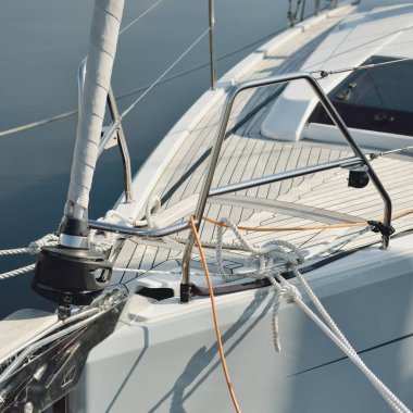 Beyaz modern yelkenli (kiralık ve satılık) yat limanındaki bir rıhtıma demirlemiş. Tahta meşe güvertesi. Denizcilik, ulaşım, amatör yelkencilik, tatiller, gezinti, eğlence kavramları