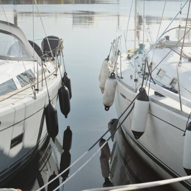 Beyaz modern yelkenli (kiralık ve satılık) yat limanındaki bir rıhtıma demirlemiş. Deniz aracı, ulaşım, amatör yelkencilik, spor, boş zaman aktivitesi, tatiller, gezinti, eğlence kavramları.