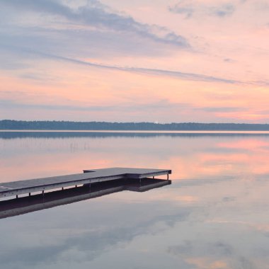 Gün batımında Orman Gölü. Ahşap iskele. Yumuşak güneş ışığı, parlayan bulutlar kristal berrak suda simetri yansımaları. Idyllic manzara. Panoramik manzara. Doğa, ekoloji, çevrecilik. Barış ve neşe kavramları