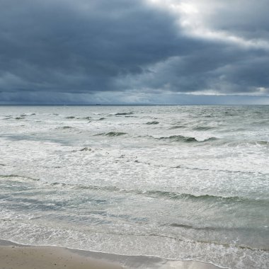Baltic sea during the storm. Dramatic sky, dark glowing clouds. Waves, water splashes. Idyllic seascape. Climate change, nature, fickle weather, ecology