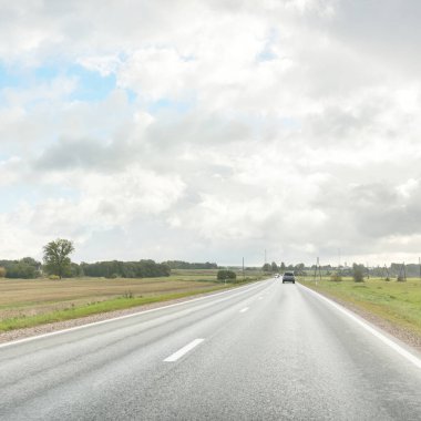 Tarlalar ve orman boyunca (asfalt yol) yol. Arabadan bak. Dramatik fırtına bulutları. Seyahat yerleri, rotalar, tatiller, lojistik, uzak yerler