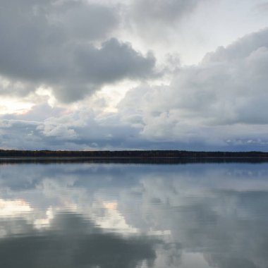 Gün batımında Orman Nehri (Lake). Dramatik gökyüzü, karanlık, parlak bulutlar. Kristal berrak suda simetri yansımaları. Panoramik sonbahar manzarası. Doğa, çevre, ekoloji, hava durumu, iklim değişikliği