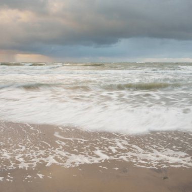 Baltic sea at sunset. Dramatic sky, blue and pink glowing clouds, golden sunlight. Waves, splashing water. Picturesque scenery, seascape, nature. Panoramic view, long exposure