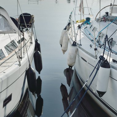 Beyaz modern yelkenli (kiralık ve satılık) yat limanındaki bir rıhtıma demirlemiş. Deniz aracı, ulaşım, amatör yelkencilik, spor, boş zaman aktivitesi, tatiller, gezinti, eğlence kavramları.