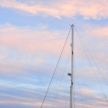 Yelkenli bir yatın direğinin alçak açılı görüntüsü. Yumuşak güneş ışığı, parlayan günbatımı gökyüzü. Ulaşım, eğlence, eğlence, gezi, spor, yelkencilik, yarış, yat