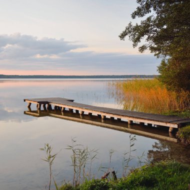 Orman Gölü (nehir) gün batımında. Ahşap iskele. Parlayan bulutlar, durgun ve berrak suda simetri yansımaları. Idyllic manzara. Doğa, ekoloji, ekolojik rezerv, eko-turizm, yürüyüş, tatiller