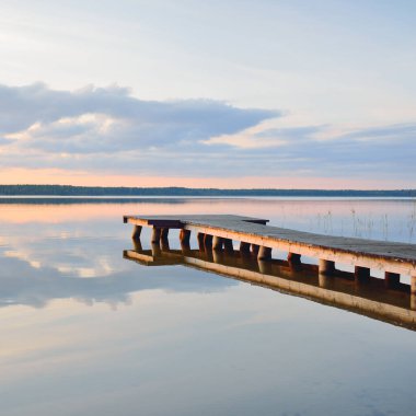Forest lake (river) at sunset. Wooden pier. Glowing clouds, symmetry reflections in a still crystal clear water. Idyllic landscape. Nature, ecology, ecological reserve, ecotourism, hiking, vacations